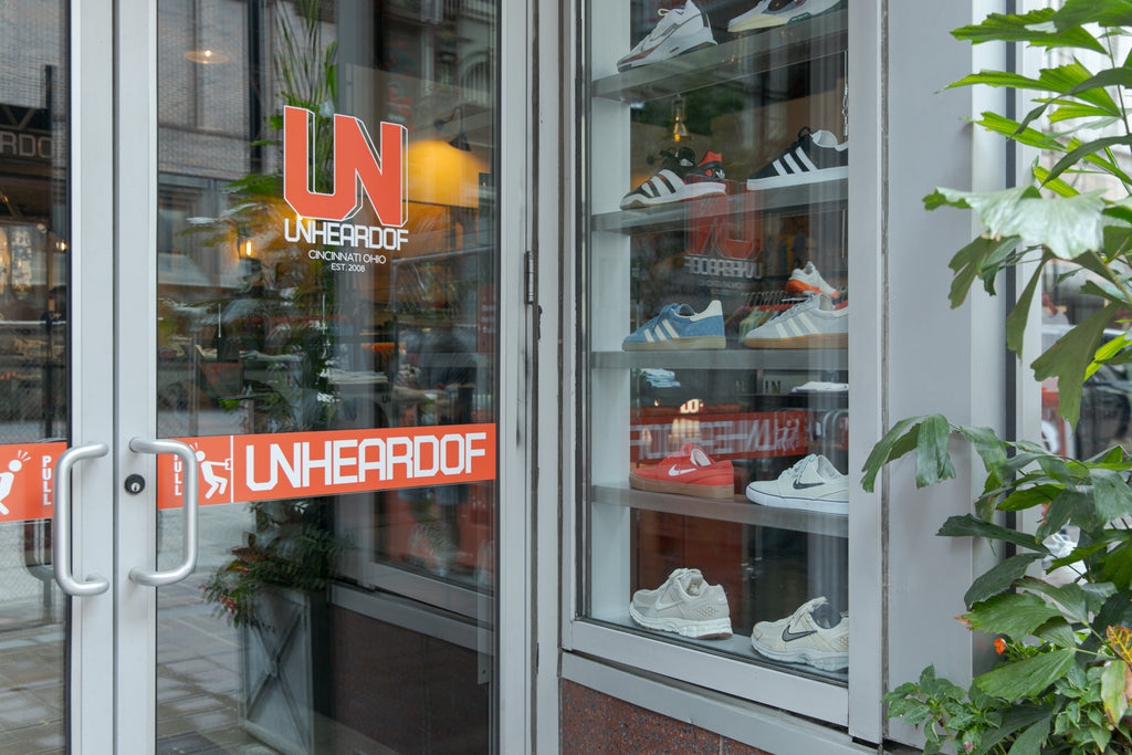 Glass entrance door of the Unheardof Brand store in Downtown Cincinnati, decaled with 'Unheardof, Cincinnati Ohio, Est. 2008' beside a sneaker display case.